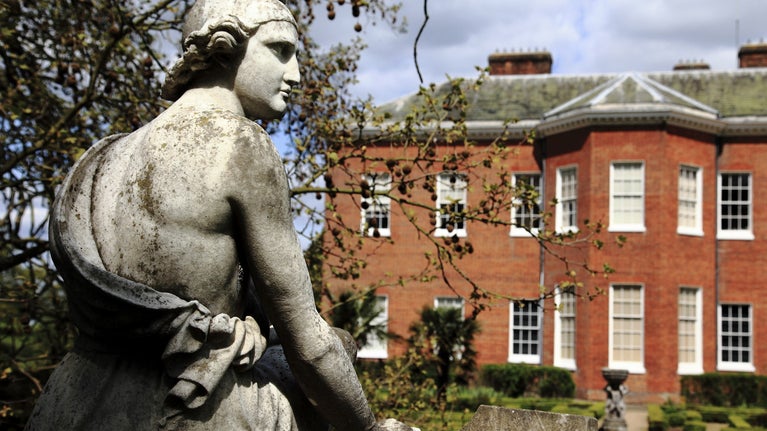 A wistful looking stone statue of "Paris", sitting on a lichen covered plinth in the grounds of Hatchlands Park, Surrey